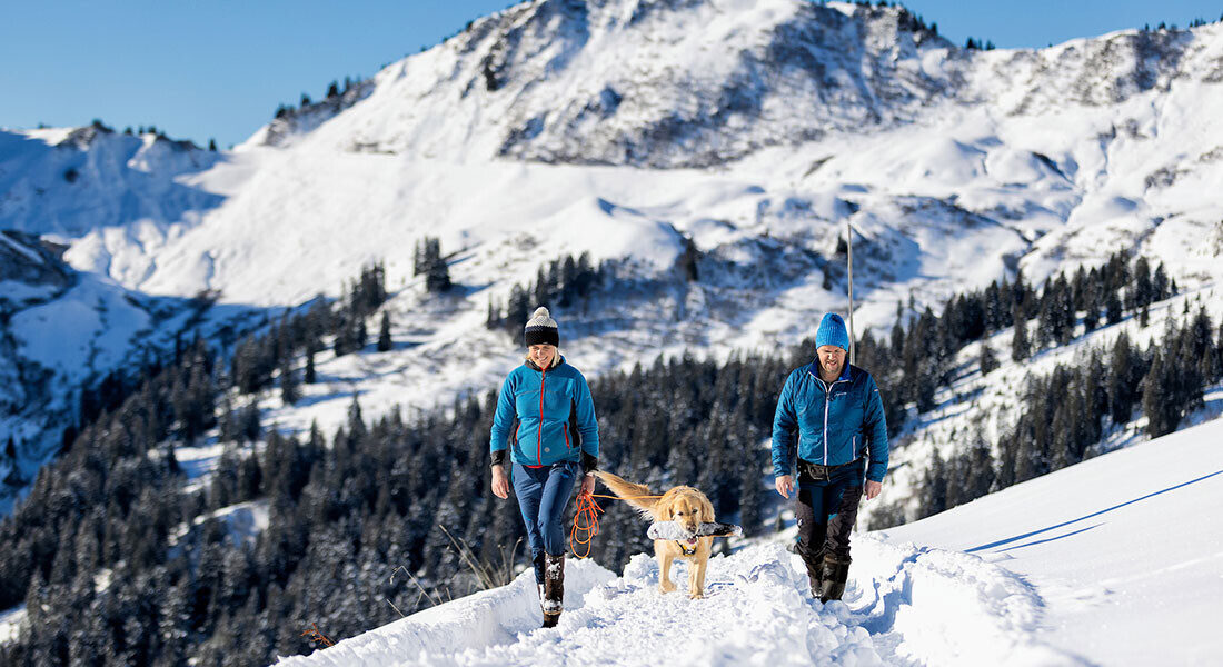 The hosts Peter and Silvia with their dog Luke walking through the snowy landscape of Faschina.