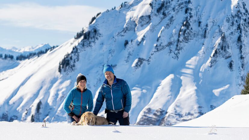 Die Gastgeber Peter und Silvia mit Hund Luke beim Spaziergang durch die verschneite Landschaft von Faschina.