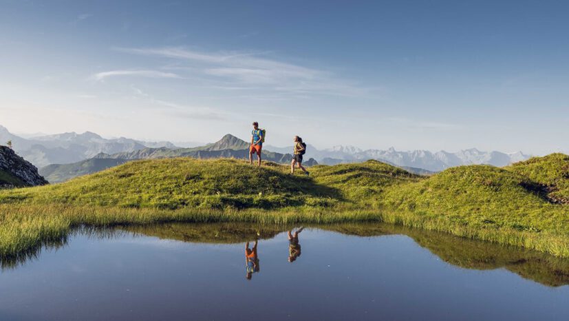 Zwei Wanderer laufen an einem See in Faschina vorbei.